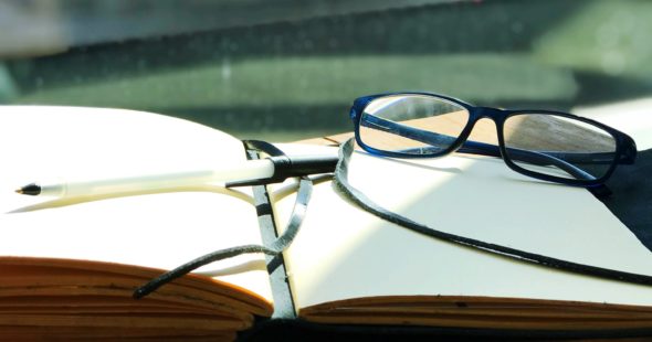 Photography of a pair of glasses, a ballpoint pen and open journal