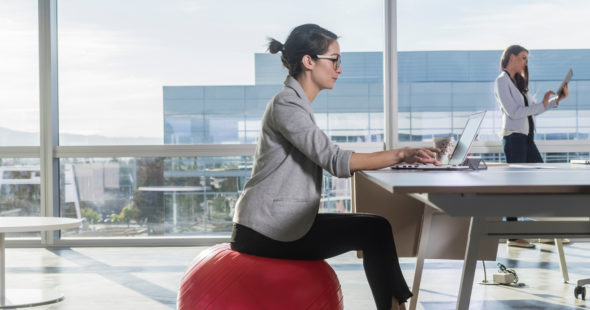 Woman sitting on a yoga ball at her desk with KINETIC®branded weights nearby
