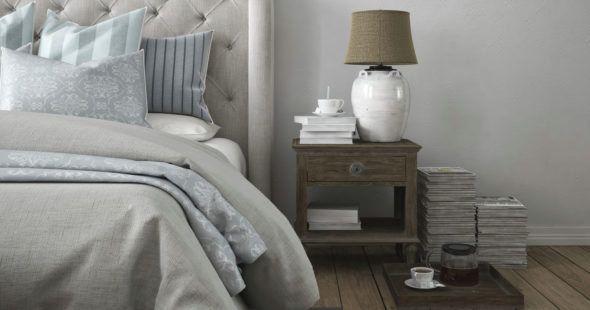 Photography of a bedroom and nightstand with a lamp, a stack of books, and a cup of coffee