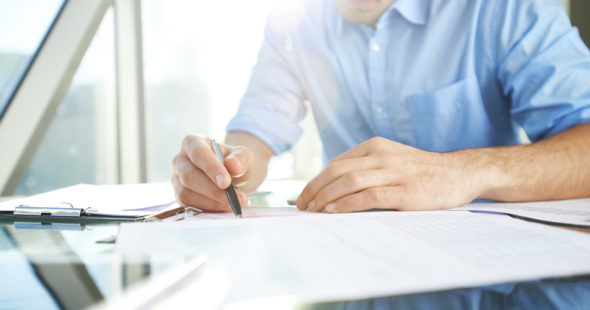 Man in a blue shirt holding a pen doing paperwork over a reflective table
